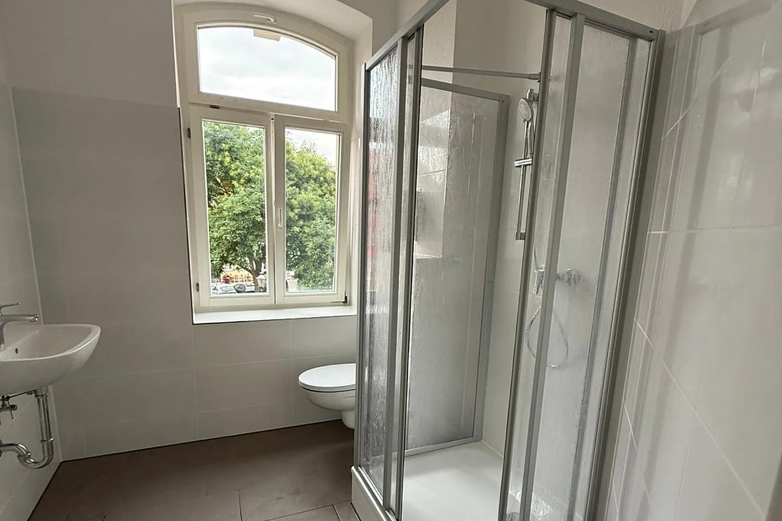 Altbaubad nach der Renovierung mit Bogenfenster, Duschkabine, Waschbecken und Wand-WC